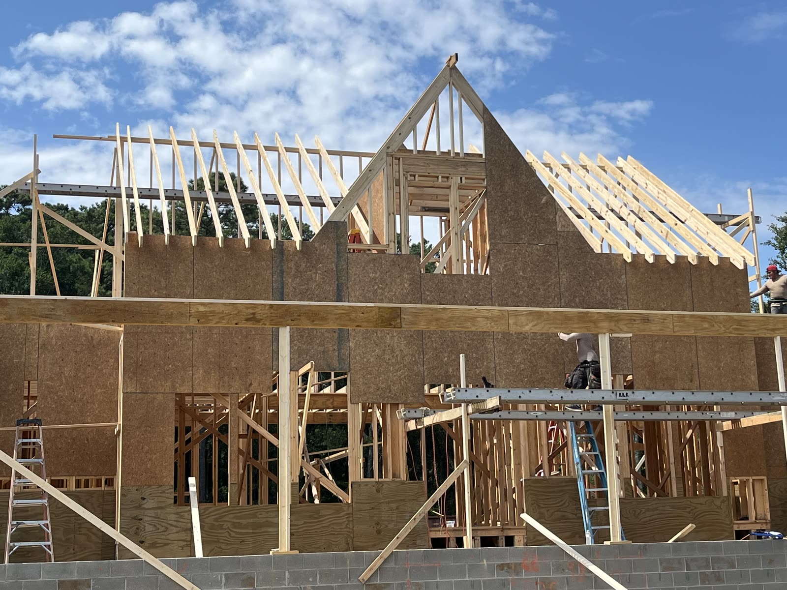 Two-story home framing in progress with crew working on wall sheathing and roof rafters